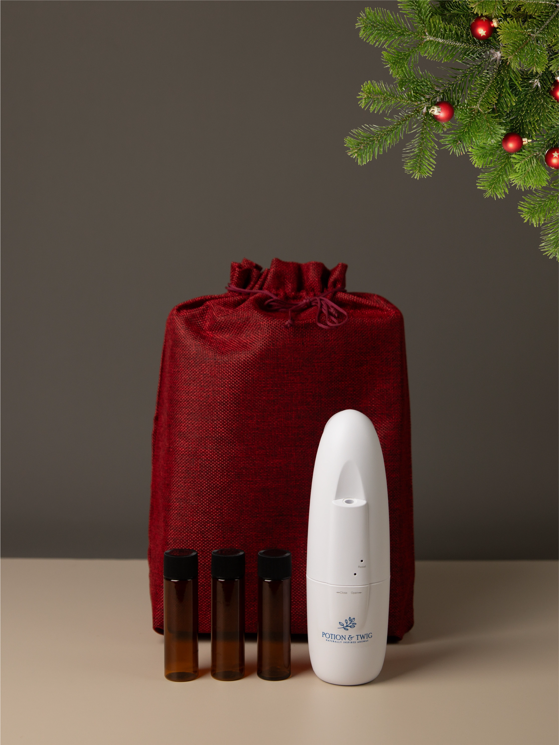 Red gift bag with a Sienna Oil Diffuser and three bottles of diffuser oil. Christmas tree limb showing in the corner.