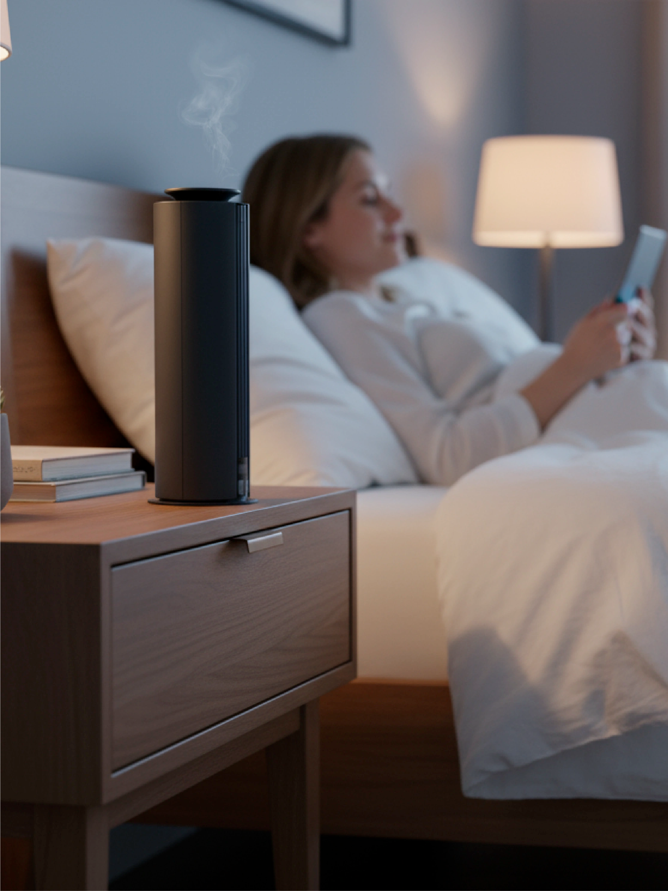 Woman lying in bed using a smartphone with a Spire wireless scent diffuser on the nightstand.