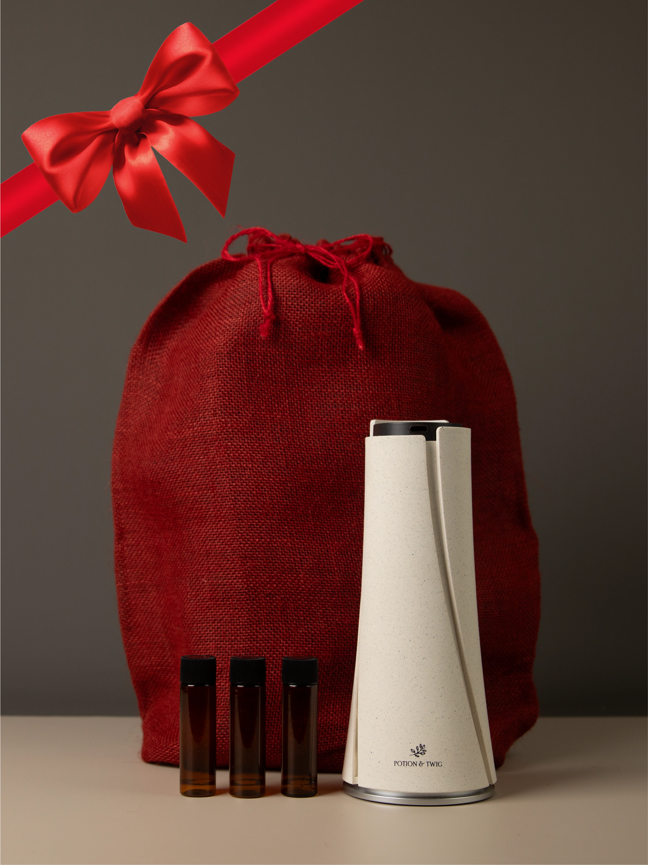 Red gift bag with a red ribbon with a Lumen Oil Diffuser and three bottles of diffuser oil