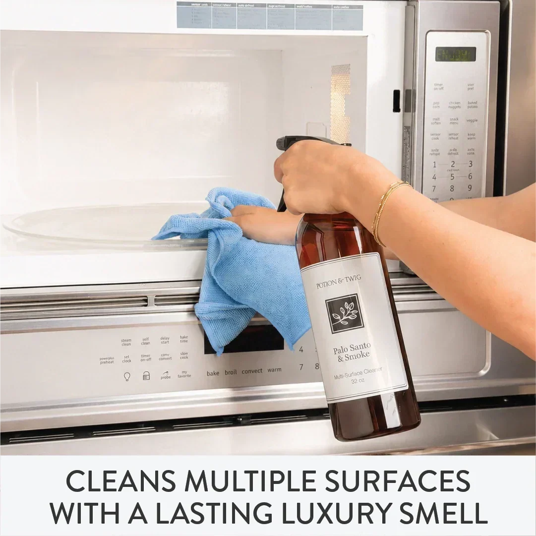 Person cleaning a microwave with a bottle of cleaning solution branded "Potion & Twig"