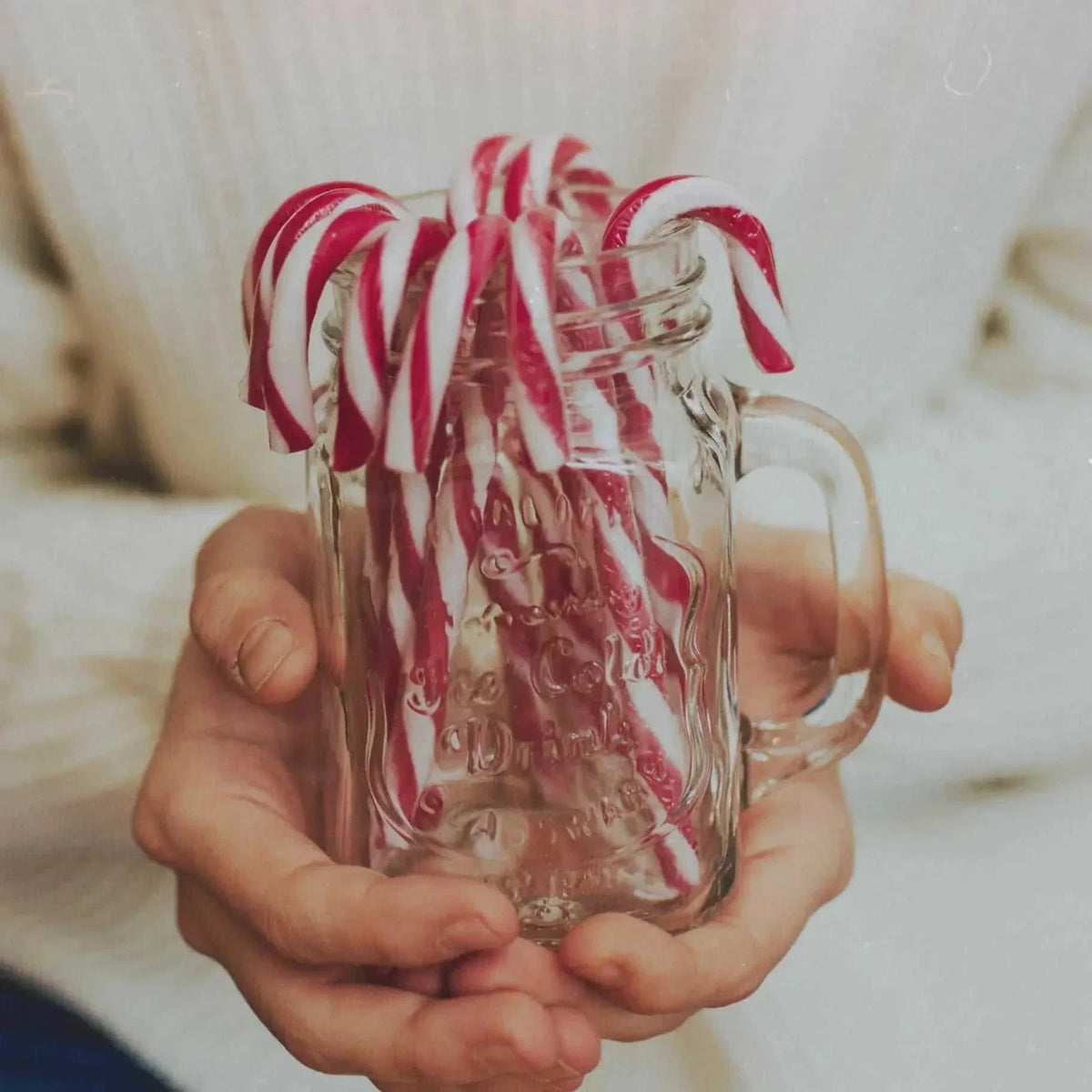 Candy Cane fragrance represented by red and white striped peppermint sticks arranged inside a clear glass mug