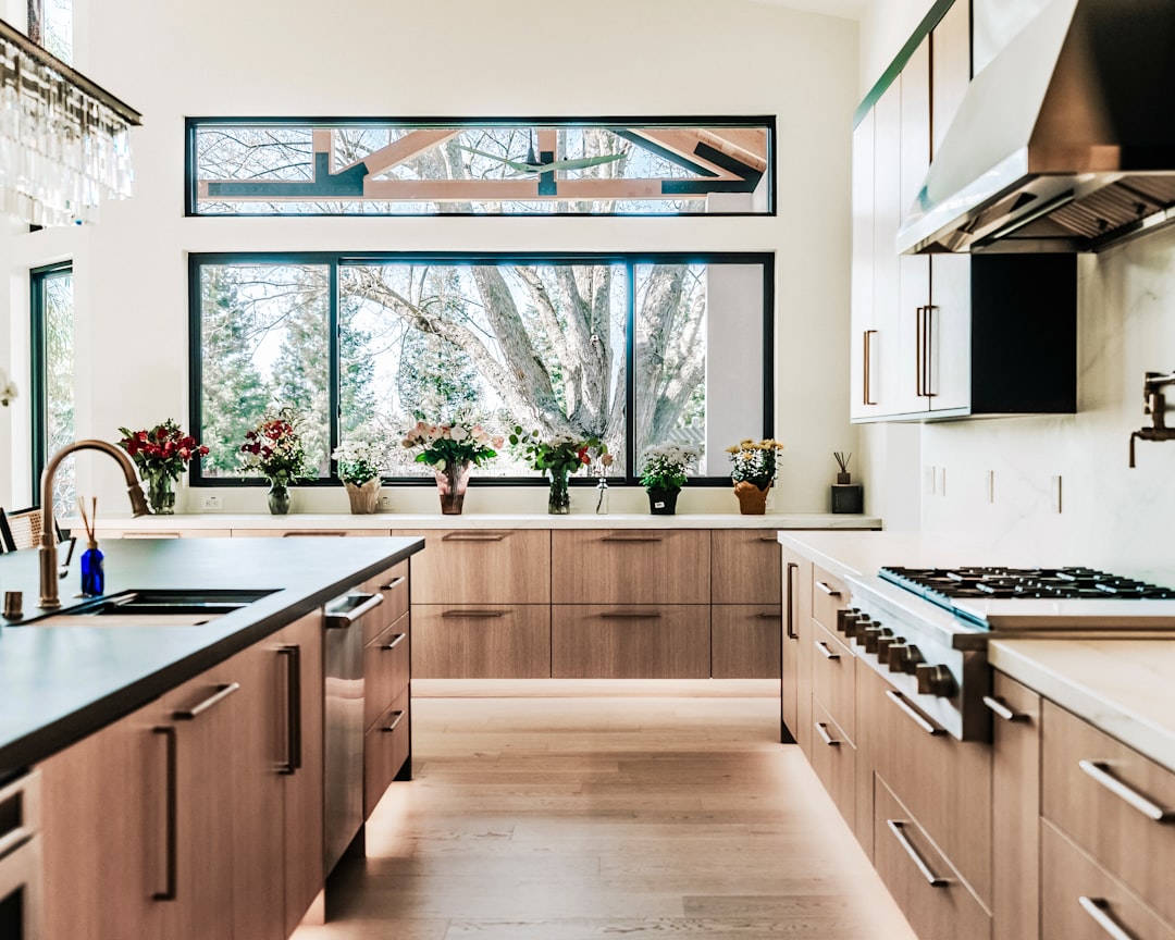 Very clean luxurious modern kitchen. With large window and vases of flowers sitting on the window