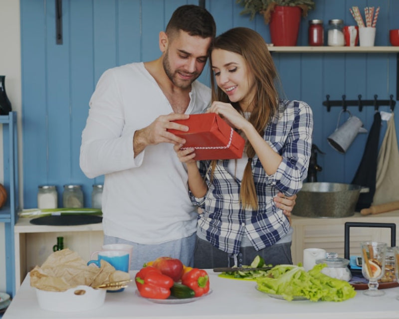 Young married couple in the kitchen both looking at a wrapped gift together
