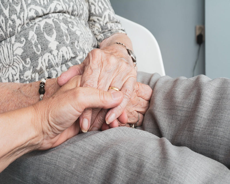 Two pairs of hands holding each other, one older and one younger, against a neutral background.