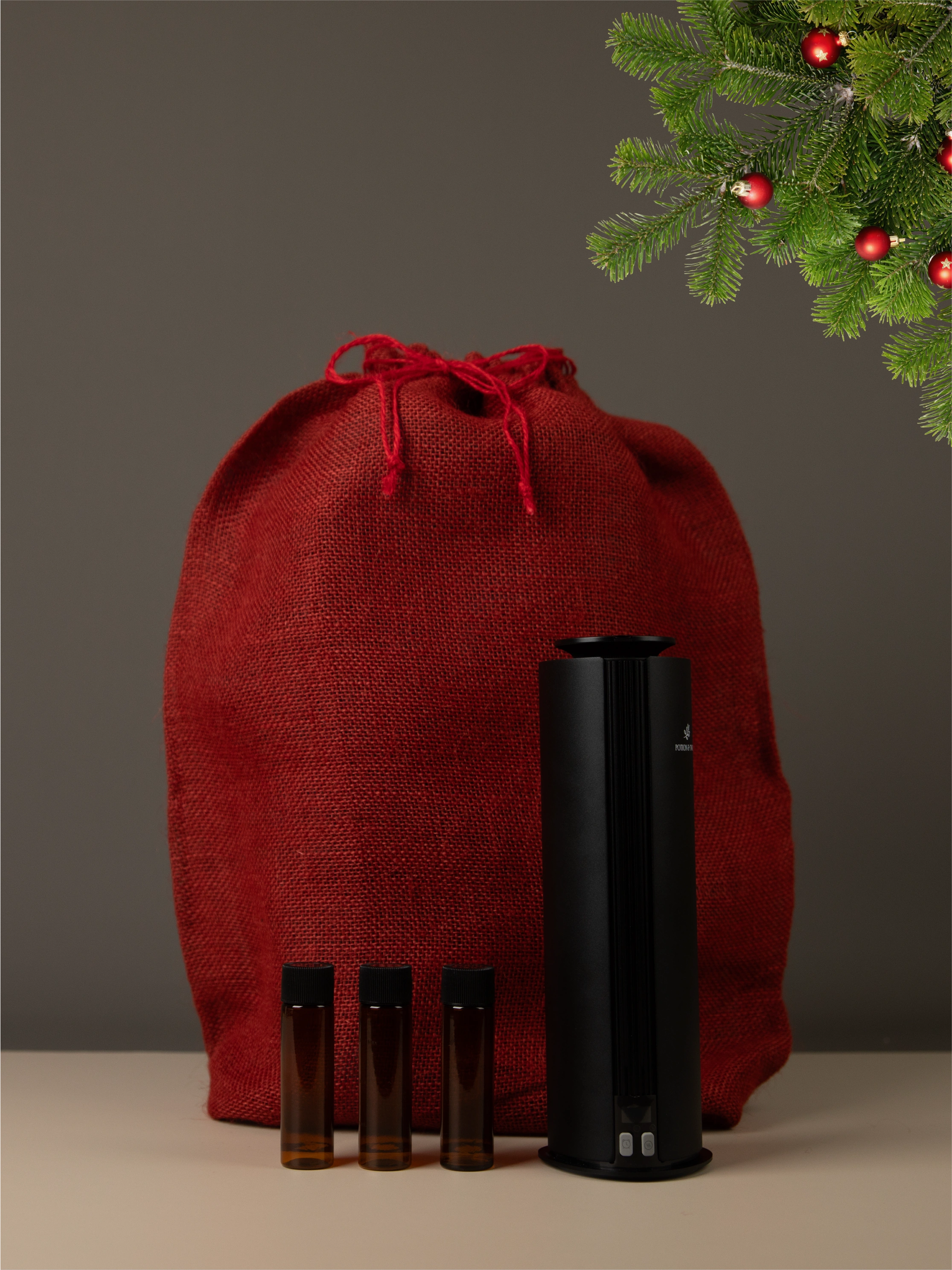 Red drawstring bag with black Spire diffuser and three brown bottles of diffuser oil on a neutral background