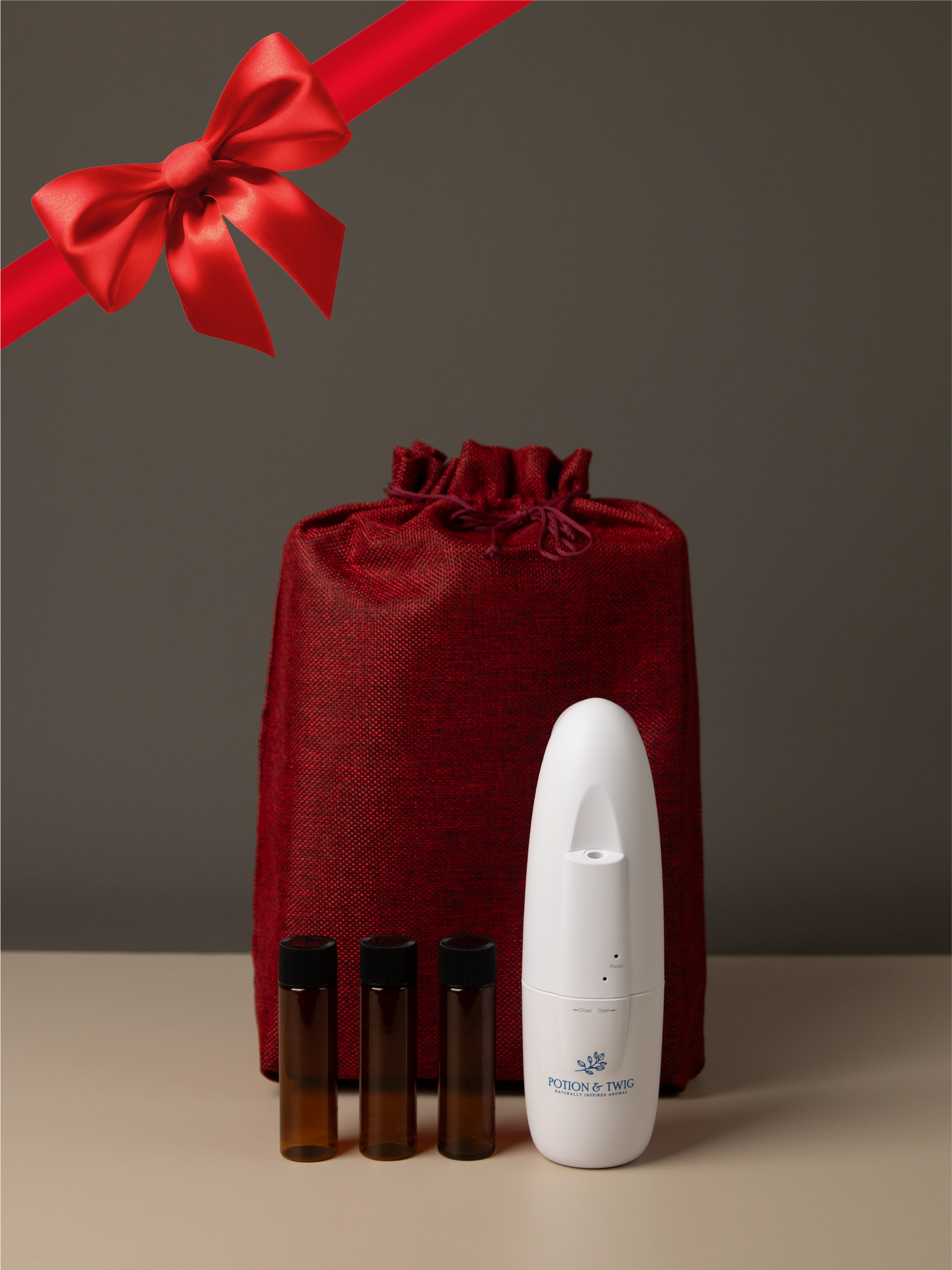 Red gift bag with a Sienna Oil Diffuser and three bottles of diffuser oil. Red bow and ribbon showing in the corner.