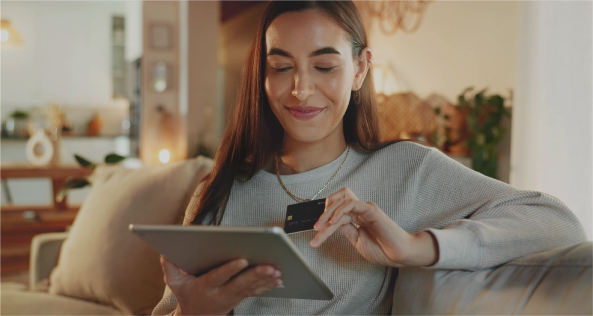 Woman using a tablet and credit card in a cozy living room.