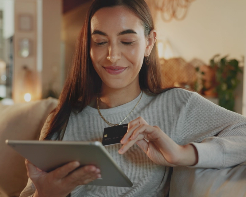 Woman holding a tablet and a credit card in a cozy indoor setting