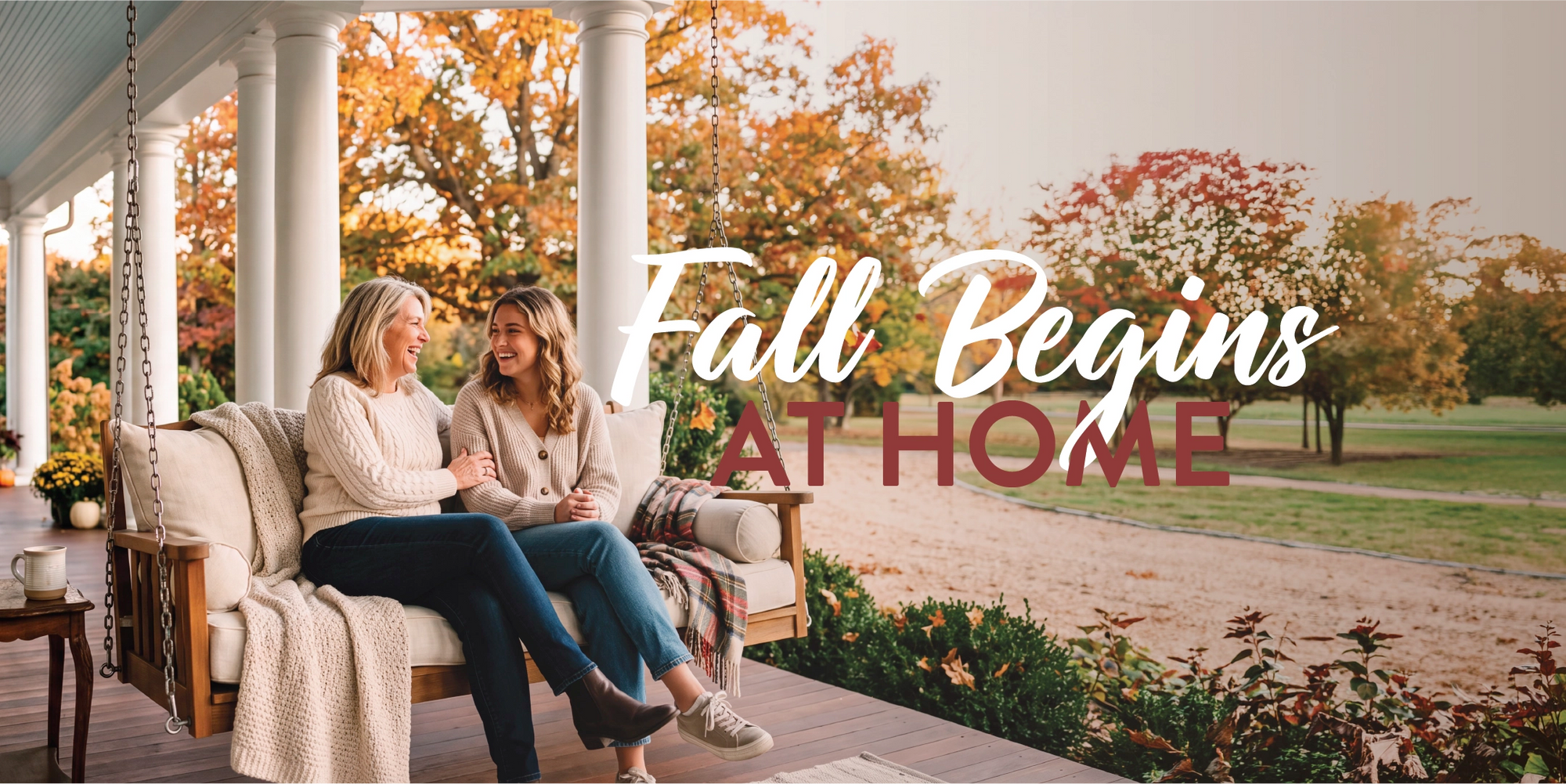 Two women sitting on a porch swing on a country-style home porch, with autumn trees in the background and the text 'Fall Begins AT HOME' overlaid across the center.