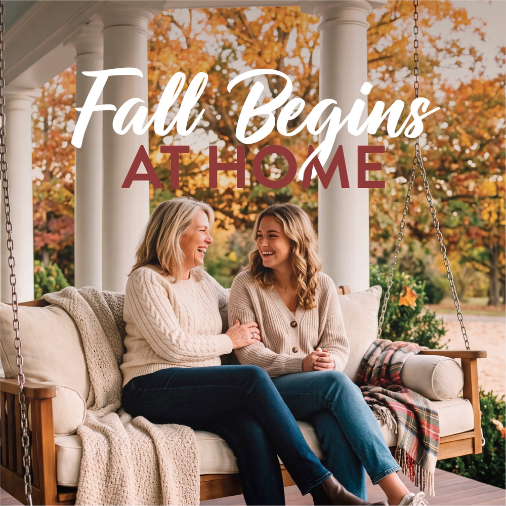 Two women sitting together on a porch swing in front of a fall garden, with the text 'Fall Begins AT HOME' overlaid across the top.