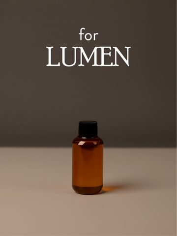 Amber diffuser oil bottle with black cap on a gray background, featuring 'for LUMEN' text.