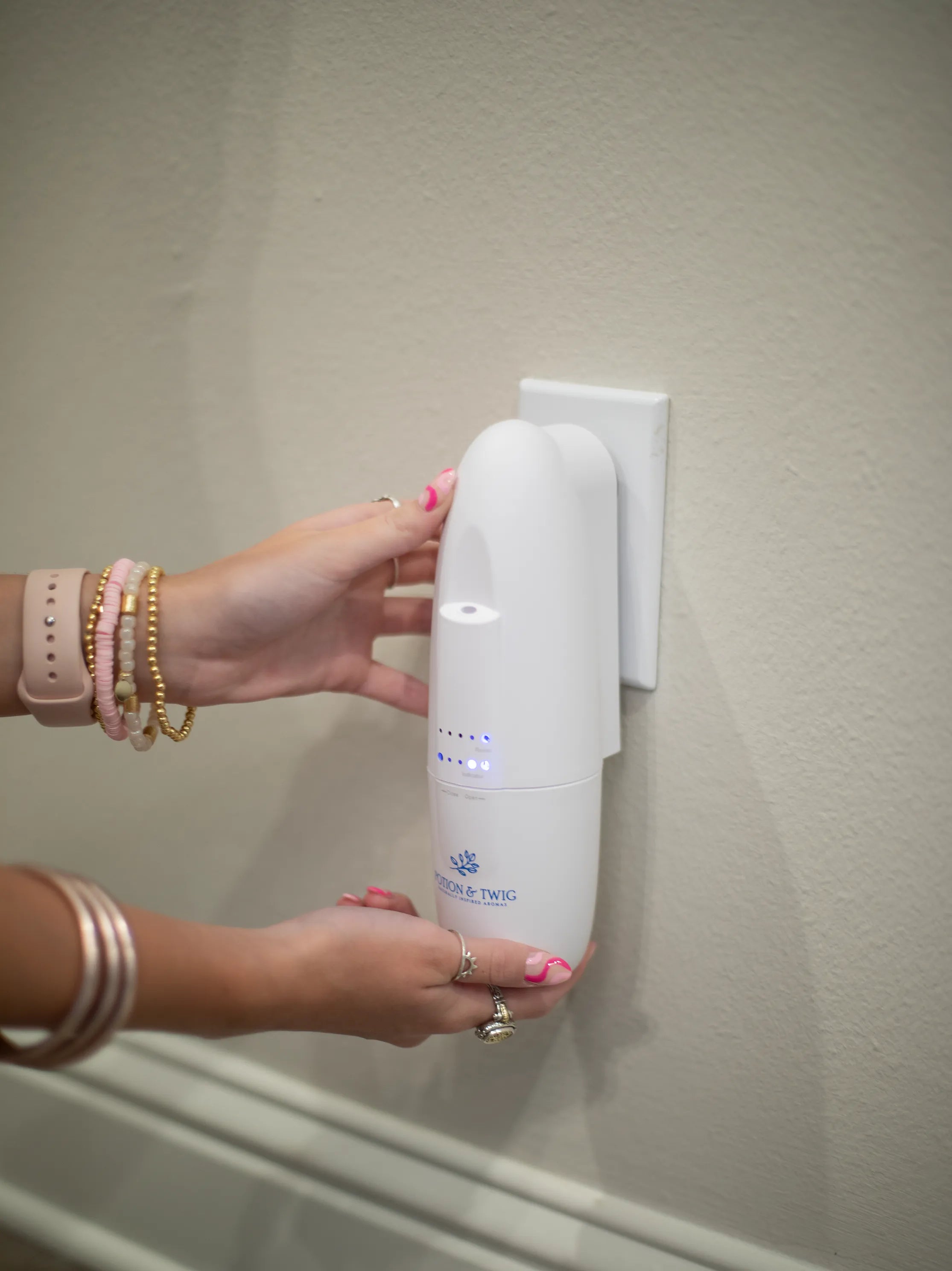 Hand holding a white wall-mounted diffuser against a beige wall.