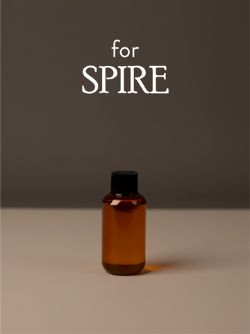Amber diffuser oil bottle with black cap on a gray background, featuring the text 'for SPIRE'.