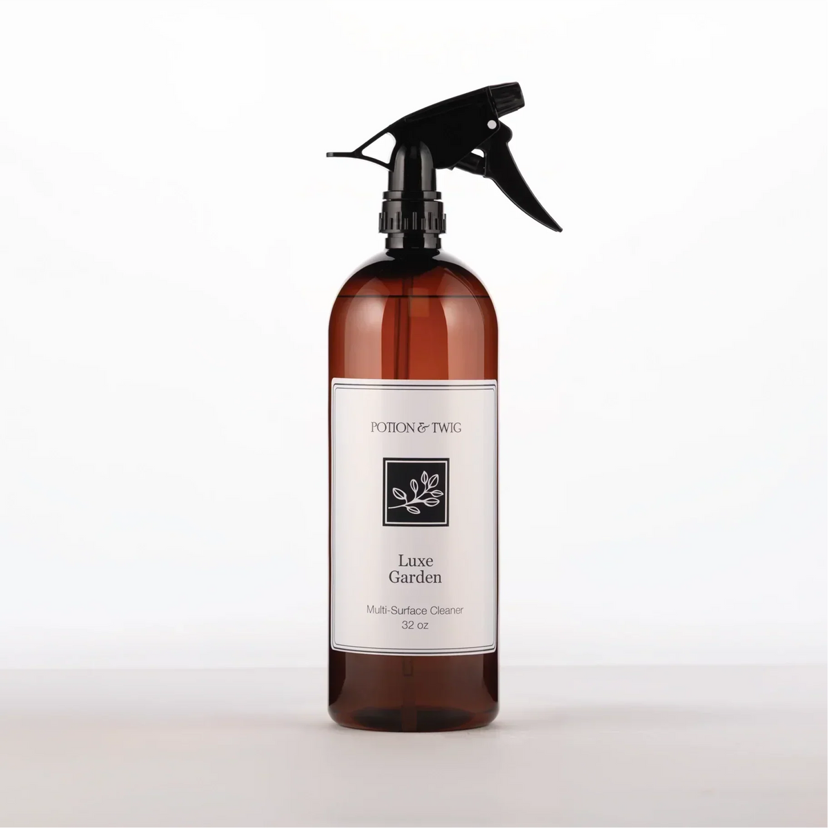 Luxury Surface Cleaner in an amber bottle with a black trigger sprayer and a white botanical label marked Luxe Garden