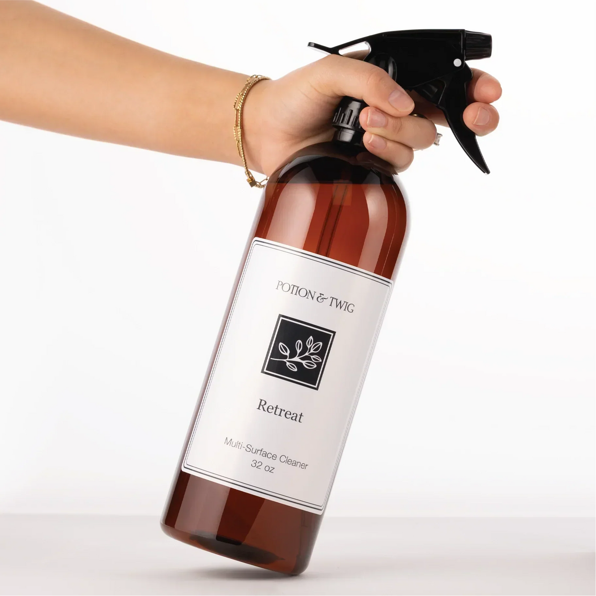 Luxury Surface Cleaner in a translucent amber bottle with a black trigger sprayer and white Retreat label