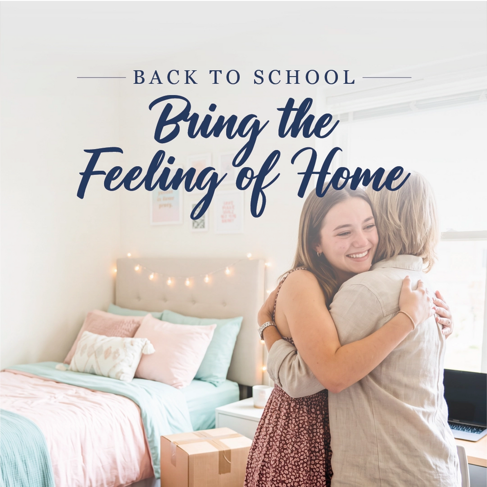 A smiling woman hugs another person in a bright bedroom, with the text 'BACK TO SCHOOL Bring the Feeling of Home' overlaid at the top. The room has a bed with pastel bedding, string lights, and a cardboard box on the floor.
