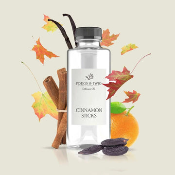 Spiced cinnamon diffuser oil in a clear bottle with a black cap, cinnamon sticks, orange and autumn leaves