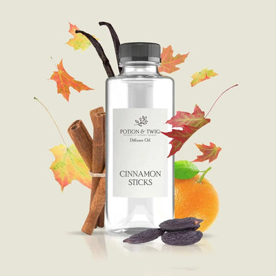 Spiced cinnamon diffuser oil in a clear bottle with a black cap, cinnamon sticks, orange and autumn leaves